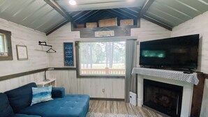 Una sala de estar acogedora con un sofá azul, una chimenea, un televisor y una ventana con vistas a árboles.