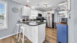 Una cocina moderna con armarios blancos, una isla central con taburetes, electrodomésticos de acero inoxidable y un mueble azul.