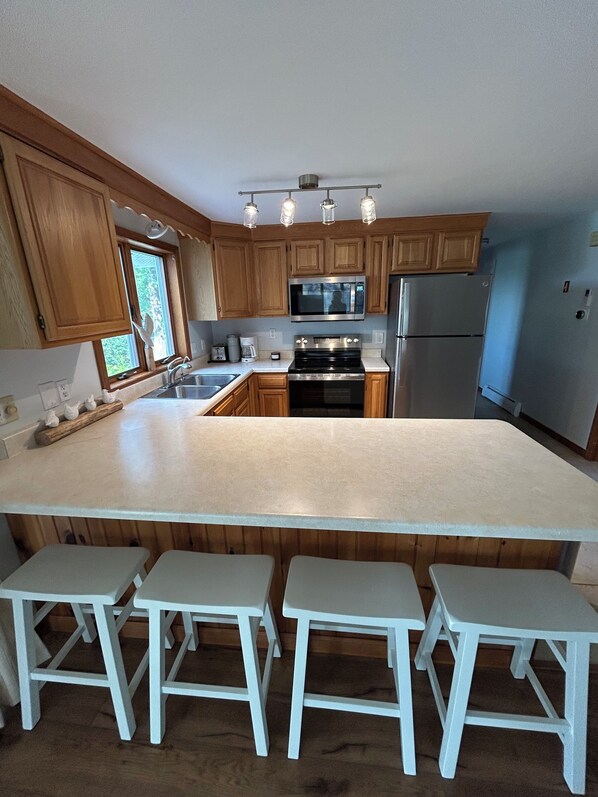 A kitchen with wooden cabinets, a large island with stools, stainless steel appliances, and a window with a view. - The MARSH LIFE. (Wells)
