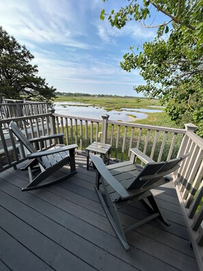 A wooden deck with two lounge chairs and a small table, overlooking a marshy landscape with water and trees. - The MARSH LIFE. (Wells)