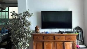 A living room with a ceiling fan, a large flat-screen TV mounted on the wall, a wooden cabinet, and a potted plant. - Casa Solana (calmar, lucena city)