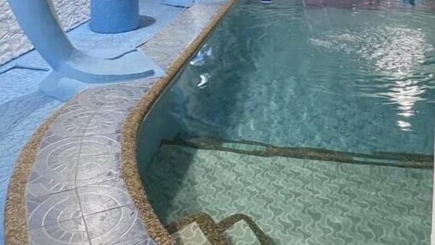 A swimming pool with a dolphin-shaped water feature, a blue cylindrical object, and a row of pink and blue slippers. - Casa Solana (calmar, lucena city)