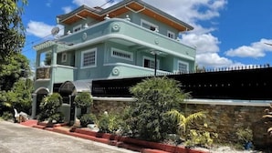 A two-story house with a light blue exterior, a stone wall, and a red curb. - Casa Solana (calmar, lucena city)