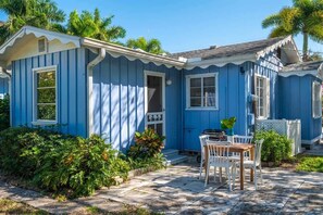 Un petit bâtiment d’un seul étage, à l’extérieur bleu, avec une porte d’entrée et un petit patio comprenant une table et des chaises.