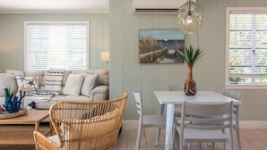 Ein gemütliches Wohnzimmer mit einer Couch, Korbsesseln, einem Esstisch und einer Hängelampe.