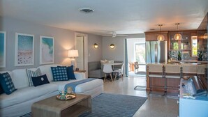 A modern living room with a sofa, coffee table, and dining area. There is a kitchen with a refrigerator and pendant lights. - Sarasota Pool Home| Hot-tub| 2-miles to Siesta (Sarasota)