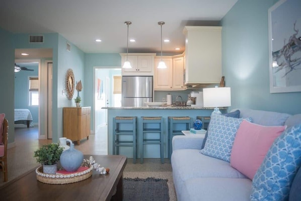 A modern kitchen with white cabinets, a stainless steel refrigerator, and a bar area with stools.