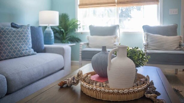 Een woonkamer met een bank, een bijzettafeltje met decoratieve objecten en een raam met uitzicht op de omgeving.