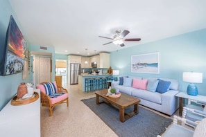 A spacious living room with a sofa, coffee table, and a dining area with a kitchen in the background.