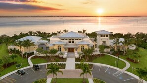 Un grand hôtel moderne doté d’une cour intérieure, entouré d’une végétation luxuriante et offrant une vue sur le coucher de soleil se reflétant sur une étendue d’eau.