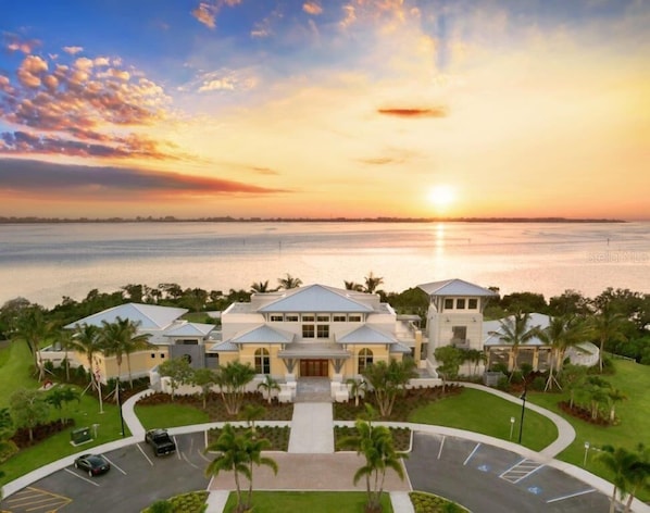 A large, modern hotel with a central courtyard, surrounded by lush greenery and a view of the sunset over a body of water.