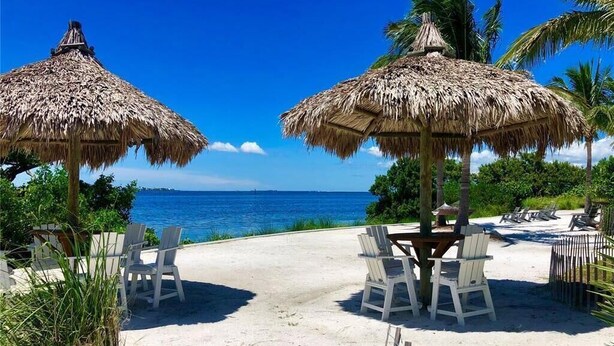 Un cadre idyllique au bord de la plage, avec des parasols en chaume, des chaises blanches et une vue sur l’océan.