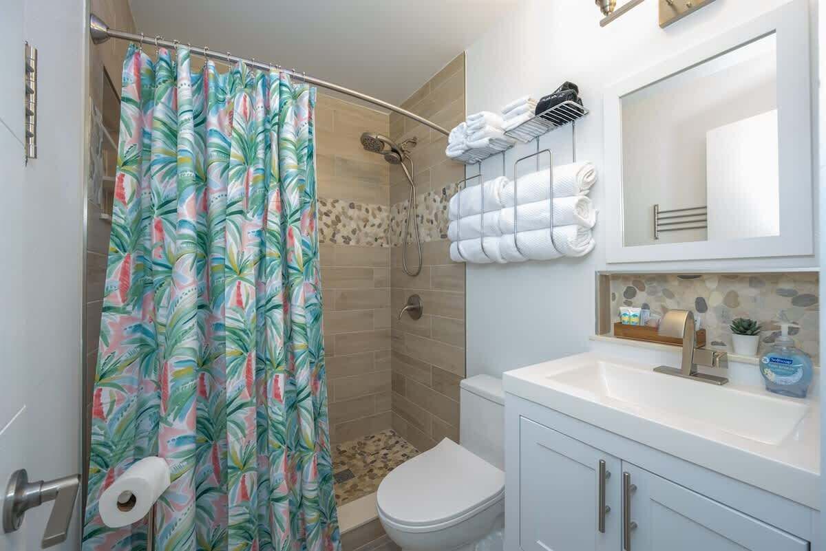 A bathroom with a shower, toilet, sink, and a towel rack with towels.