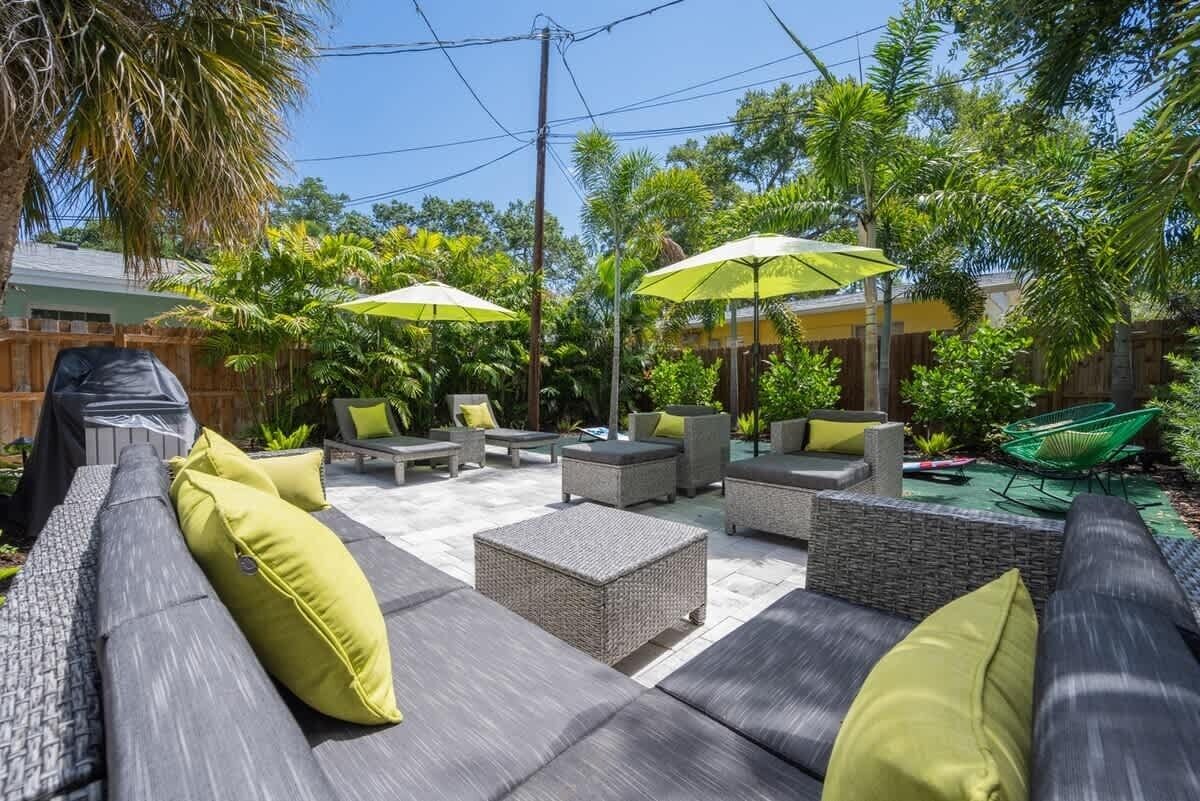 Un patio al aire libre con mobiliario de mimbre, cojines amarillos y sombrillas.