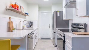 Una cocina moderna con armarios blancos, un refrigerador de acero inoxidable, un horno y una cafetera.