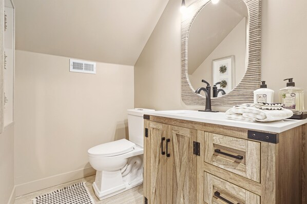 A modern bathroom with a white toilet, wooden vanity, and a large mirror.