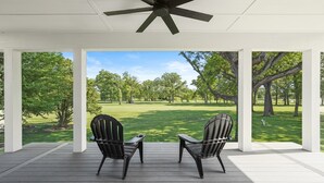 A covered porch with two Adirondack chairs facing a well-manicured lawn and trees. - Spacious 5-Bedroom Golf Course Home for Getaways (Merrillville)