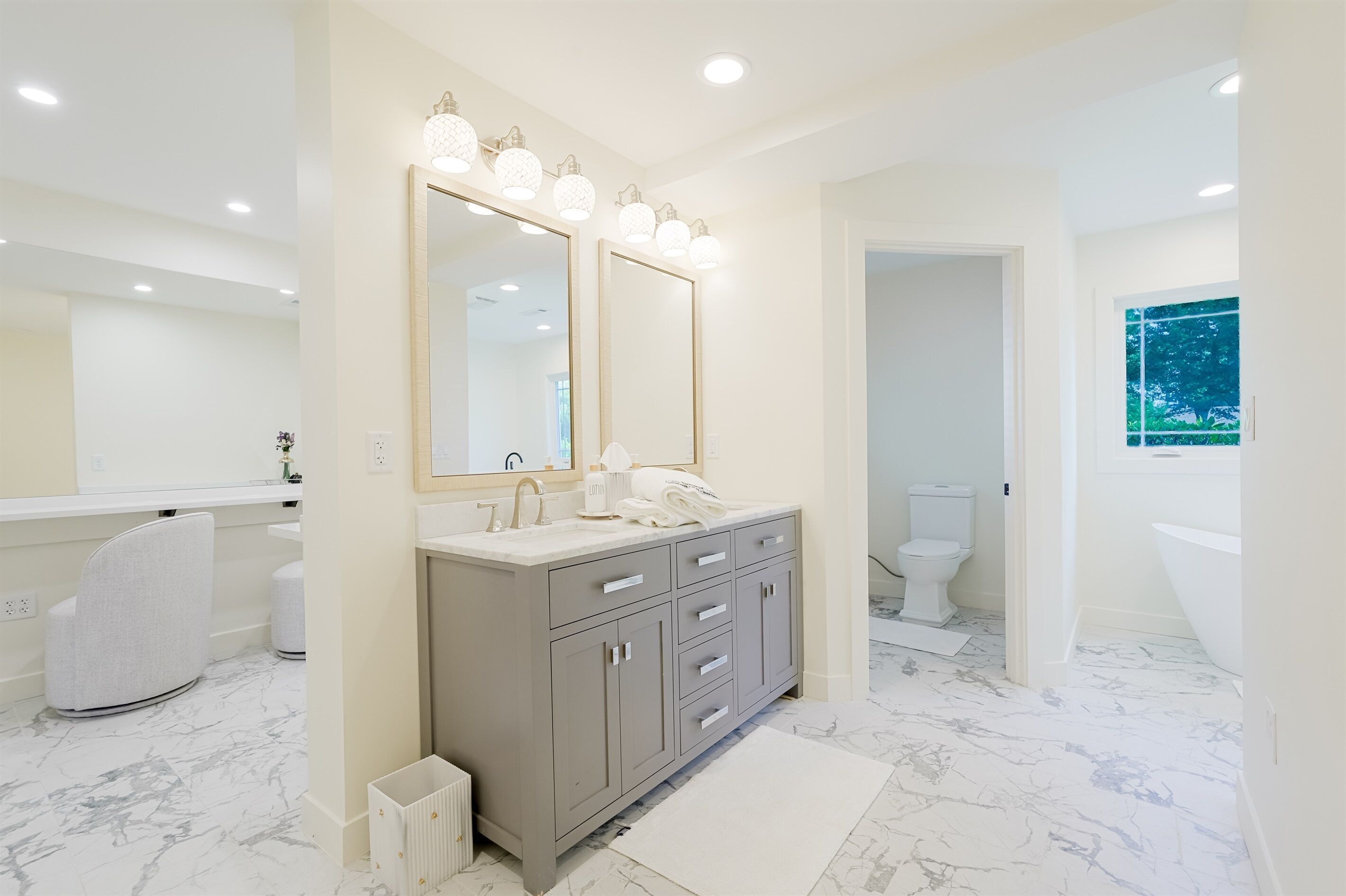 Un baño moderno con piso de mármol, un mueble de tocador amplio con espejo e iluminación, inodoro y bañera.