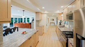 A modern kitchen with wooden cabinets, a granite countertop, stainless steel appliances, and a dining area with a view. - Spacious 5-Bedroom Golf Course Home for Getaways (Merrillville)