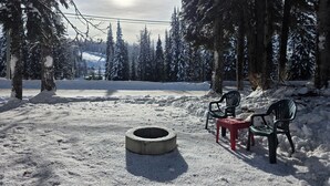A snowy outdoor area with a concrete fire pit, two black chairs, and a red chair. - A-Frame Cabin nestled in the trees - laundry, pet-friendly, close to village (Silver Star Mountain)
