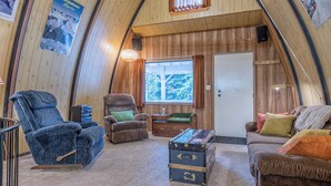 A cozy interior with a wooden ceiling, a large window, a blue reclining chair, a brown sofa, and a vintage suitcase. - A-Frame Cabin nestled in the trees - laundry, pet-friendly, close to village (Silver Star Mountain)