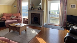 A cozy living room with a fireplace, a sofa, a television, and a view of the outdoors. - 3 bedroom house (Bushmills)