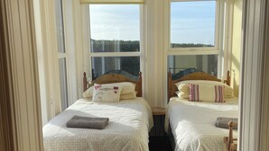 A bedroom with two beds, large windows, and a view of the outdoors. - 3 bedroom house (Bushmills)