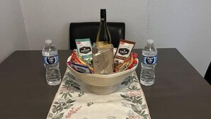A dining table with a floral tablecloth, a bowl of snacks, two bottles of water, and a bottle of wine. - Cozy & comfortable Guest house Near Hard Rock Stadium (Miami)