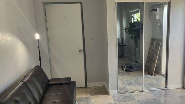 A room with a dark leather sofa, a closed door, and a sliding glass door leading to an outdoor area with a tiled floor. - Cozy & comfortable Guest house Near Hard Rock Stadium (Miami)