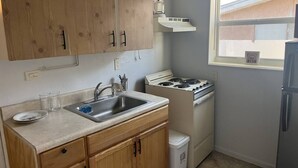 A compact kitchen with wooden cabinets, a sink, a stove, and a refrigerator. - Cozy & comfortable Guest house Near Hard Rock Stadium (Miami)
