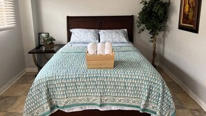 A neatly made bed with a patterned bedspread, a wooden bedside table with a plant, a framed picture of a cityscape, and a framed artwork on the wall. - Cozy & comfortable Guest house Near Hard Rock Stadium (Miami)