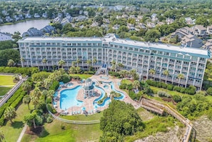 Un hotel grande con piscina central, varios balcones y abundante vegetación alrededor de la propiedad.