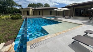 A swimming pool with blue tiles, surrounded by a patio area with lounge chairs and umbrellas. - Yeguas V18 by Wynwood House (Anapoima)