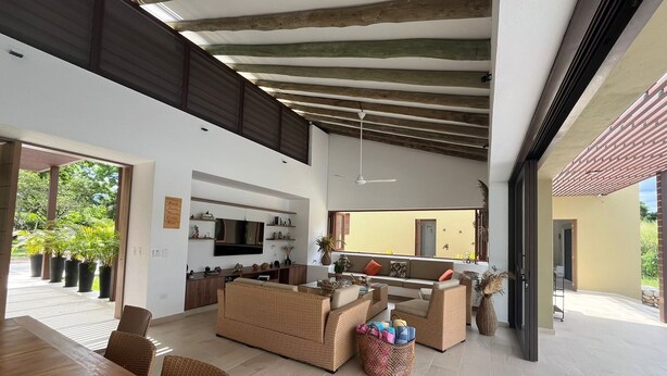 A spacious living area with a high ceiling, built-in wooden beams, a large TV, and a comfortable seating arrangement. - Yeguas V18 by Wynwood House (Anapoima)