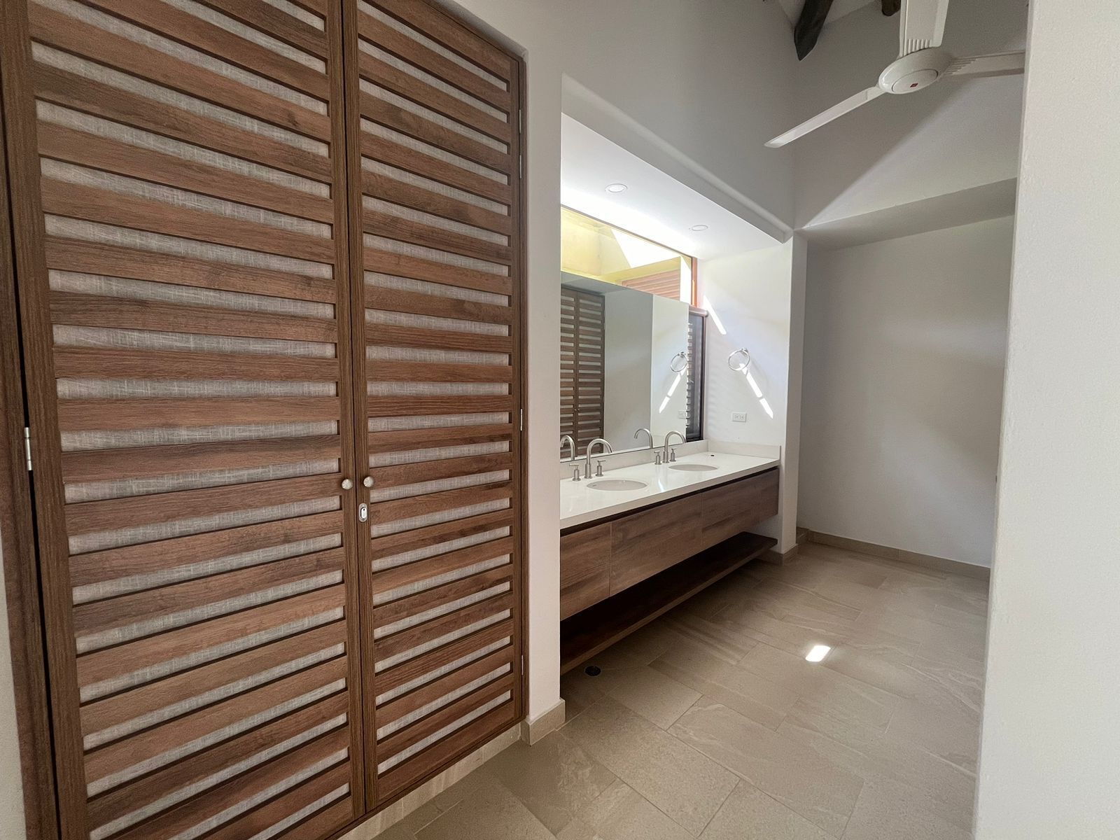 Un baño con puerta corredera de madera, tocador con espejo y ventilador de techo.