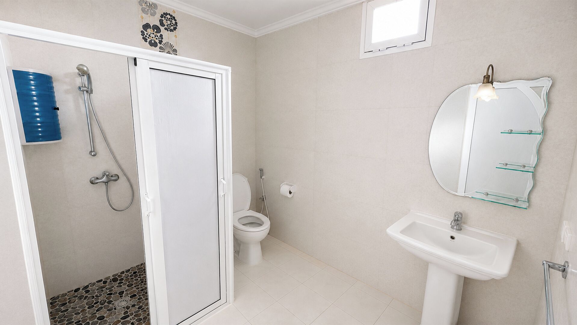 Kylpyhuone, jossa on wc, suihku, pesuallas ja peili, jonka yhteydessä on hyllyjä.
