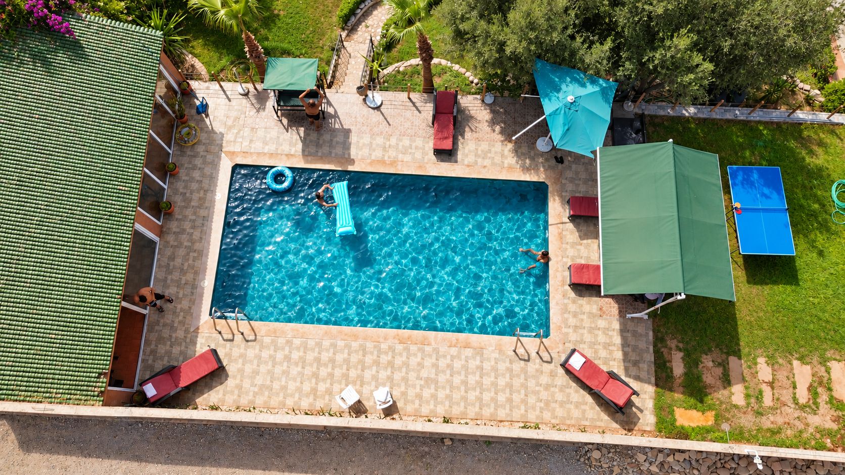 A rectangular swimming pool with a tiled deck surrounding it, equipped with lounge chairs and umbrellas.