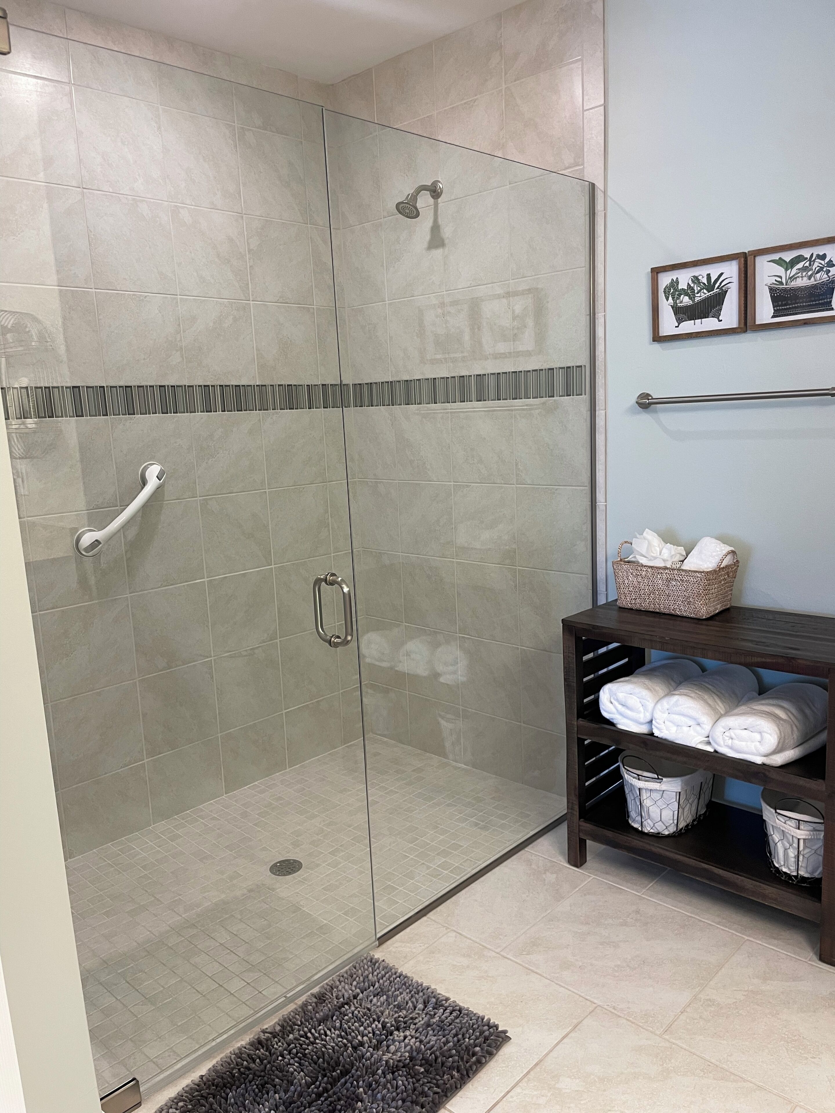 A modern bathroom with a glass-enclosed shower, a towel rack, and a shelf with towels and baskets.