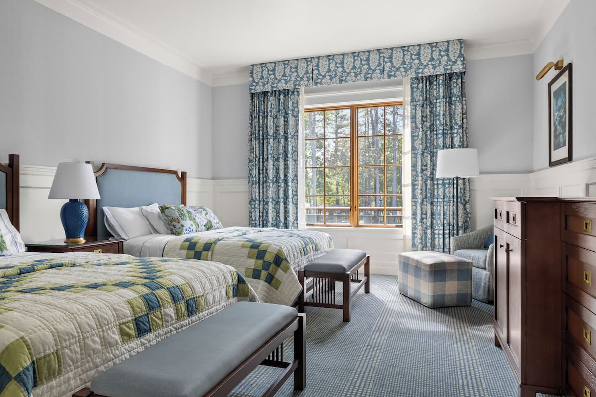 Une chambre avec deux lits, une commode, une fenêtre avec des rideaux et une lampe.