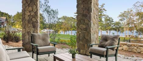 Une terrasse extérieure avec des piliers en pierre, des sièges confortables et une vue sur un lac.