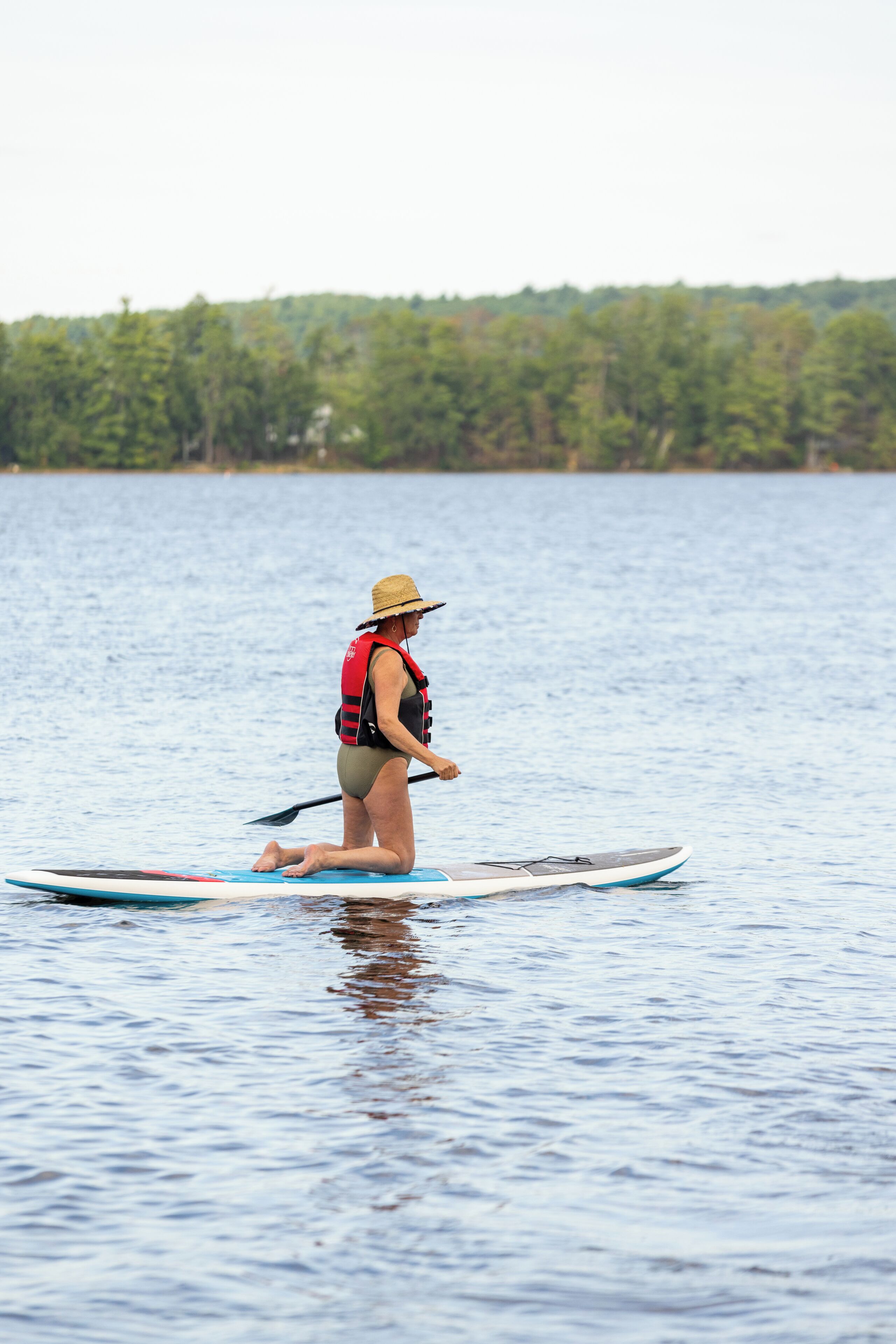 Una persona haciendo paddleboard en aguas tranquilas, con una orilla arbolada al fondo.