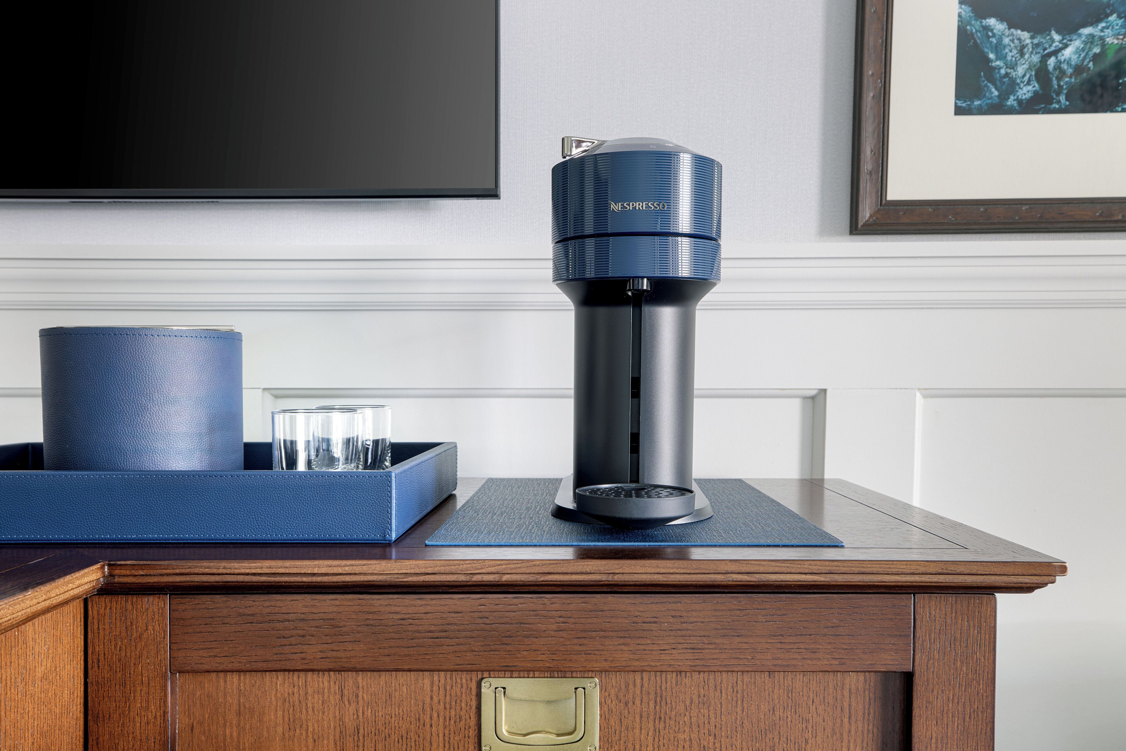 Une machine à café Nespresso posée sur une table en bois, avec un plateau bleu et des verres.