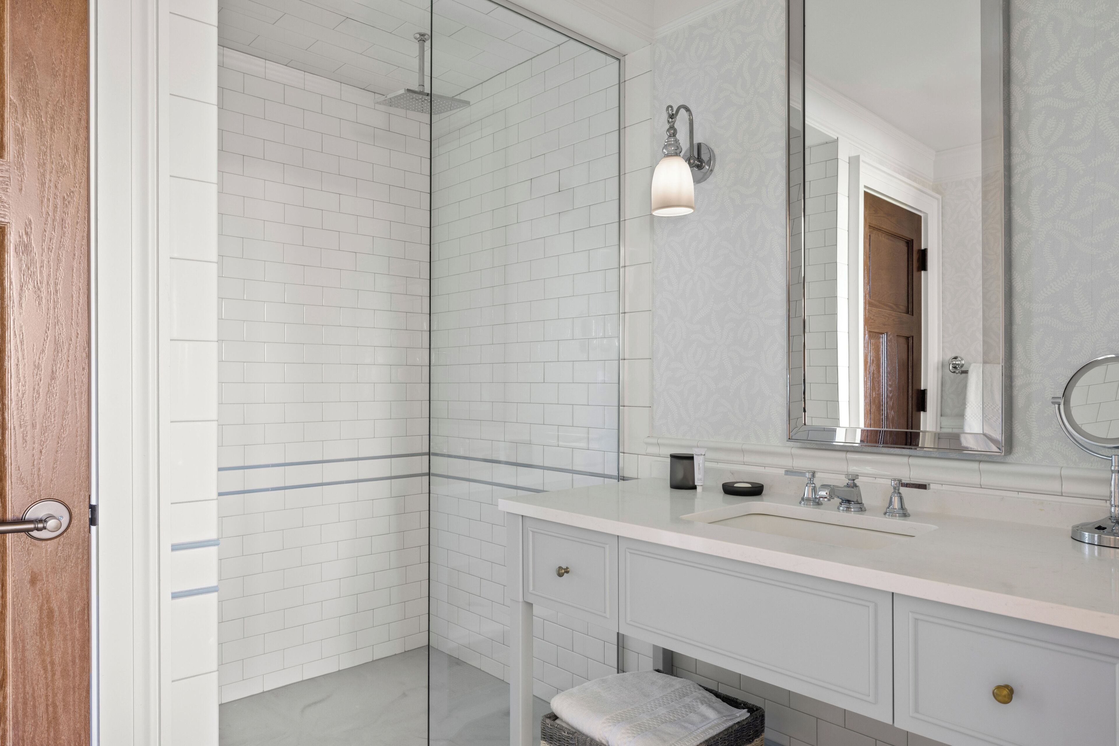 Een moderne badkamer met een douchecabine van glas, een witte wastafel met spiegel en een houten deur.