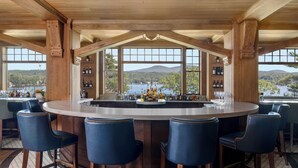 Eine Bar mit Holzbalkendecke, großen Fenstern und Blick auf See und Berge.