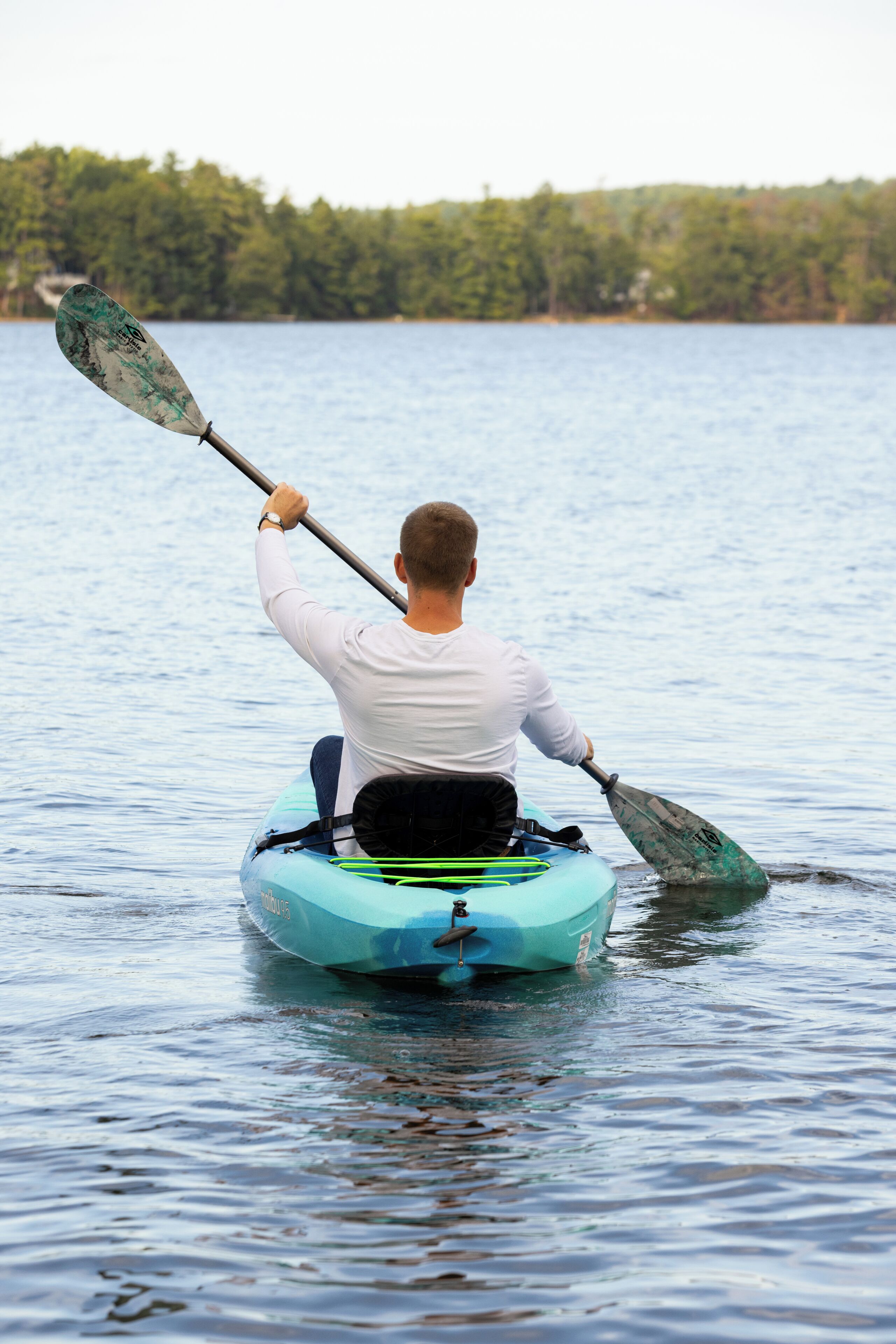 Une personne fait du kayak sur un lac paisible, avec une forêt en arrière-plan.