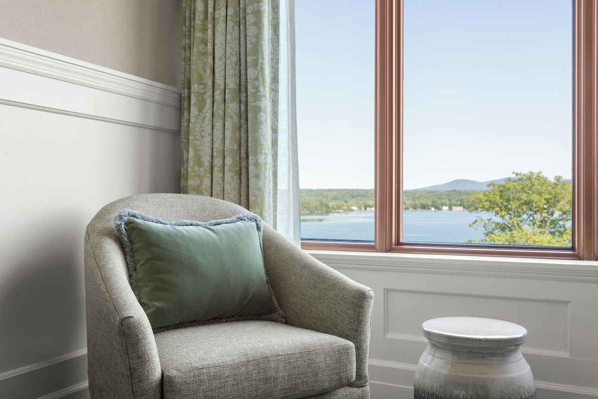 Une pièce avec vue sur un lac et des montagnes, une chaise avec un coussin et un vase posé sur une table.