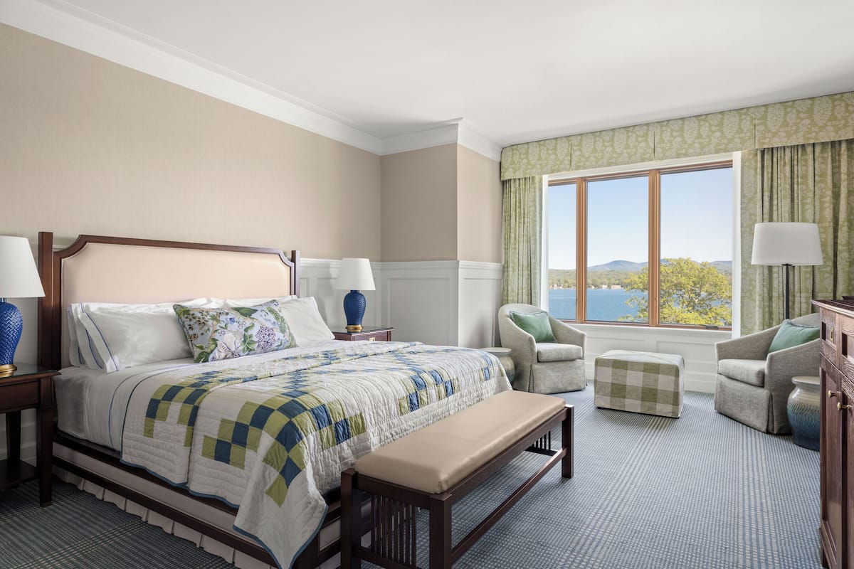 Une chambre d’hôtel avec un grand lit, deux fauteuils, un banc et une vue sur l’extérieur.