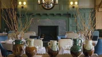 A dining area with tables set for a meal, a chandelier with candles, and vases with branches.