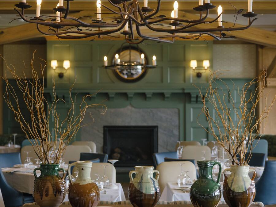 A dining area with tables set for a meal, a chandelier with candles, and vases with branches.
