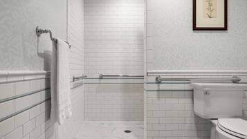 A modern bathroom with white subway tiles, a glass shower enclosure, a toilet, and a framed botanical print on the wall.